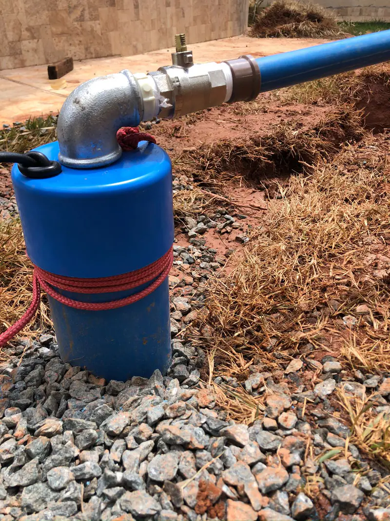 Cabeçote azul com conexão metálica e tubulação, instalado sobre brita junto ao solo.